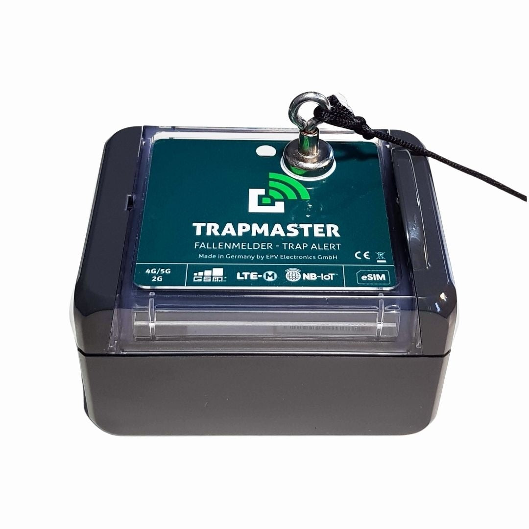 Elektronischer Fallenmelder vom Typ TRAPMASTER in schwarzem Gehäuse mit grünem Label auf der Oberseite. Zu sehen sind die Logos für LTE-M, NB-IoT, eSIM und Mobilfunknetz-Unterstützung (2G, 4G/5G). Oben befindet sich eine Öse mit montierter Schraube und Sicherungsschnur.